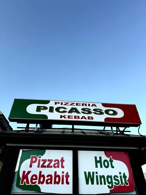 Pizzeria Picasso Kebab -kyltti vihreä–valkoinen–punaisena sinistä taivasta vasten, ikkunoissa tekstit Pizzat, Kebabit ja Hot Wingsit.